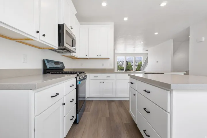 White cabinetry with matte black hardware, light-toned countertops, and wood-finish flooring