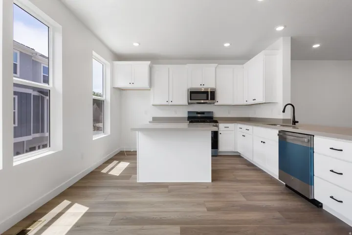 Modern kitchen featuring white cabinetry with black hardware, light-toned countertops, and wood-finish flooring
