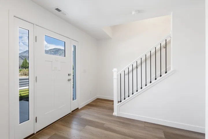 Entryway featuring a white paneled door with glass sidelights and transom, wood-finish flooring, white walls, and a staircase with white newel and handrail and black metal balusters