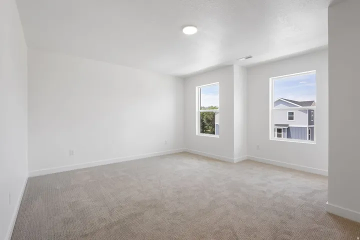 Spacious room featuring neutral carpeting, white walls, two windows, and recessed ceiling lighting