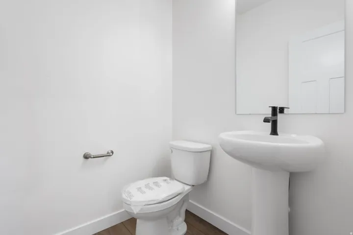 Pedestal sink with matte black faucet, full-width mirror, and wood-finish flooring