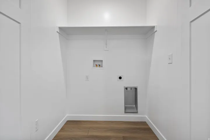 Dedicated laundry area with wood-finish flooring, white walls, and a built-in storage shelf