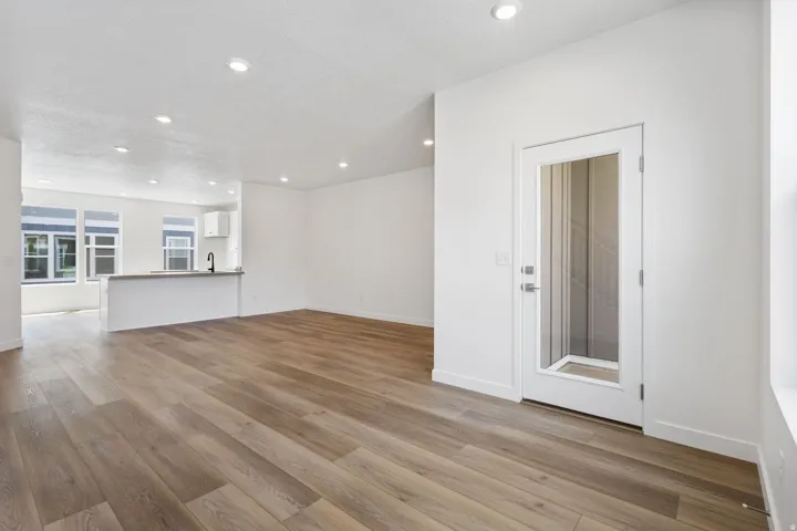 Open-concept living area featuring wood-finish flooring, recessed lighting, white walls, and a glass-paneled door