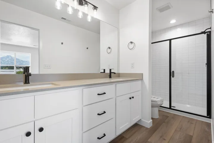 Bathroom featuring a double vanity with light-toned countertops and integrated sinks, matte black faucets, and white cabinetry with black hardware