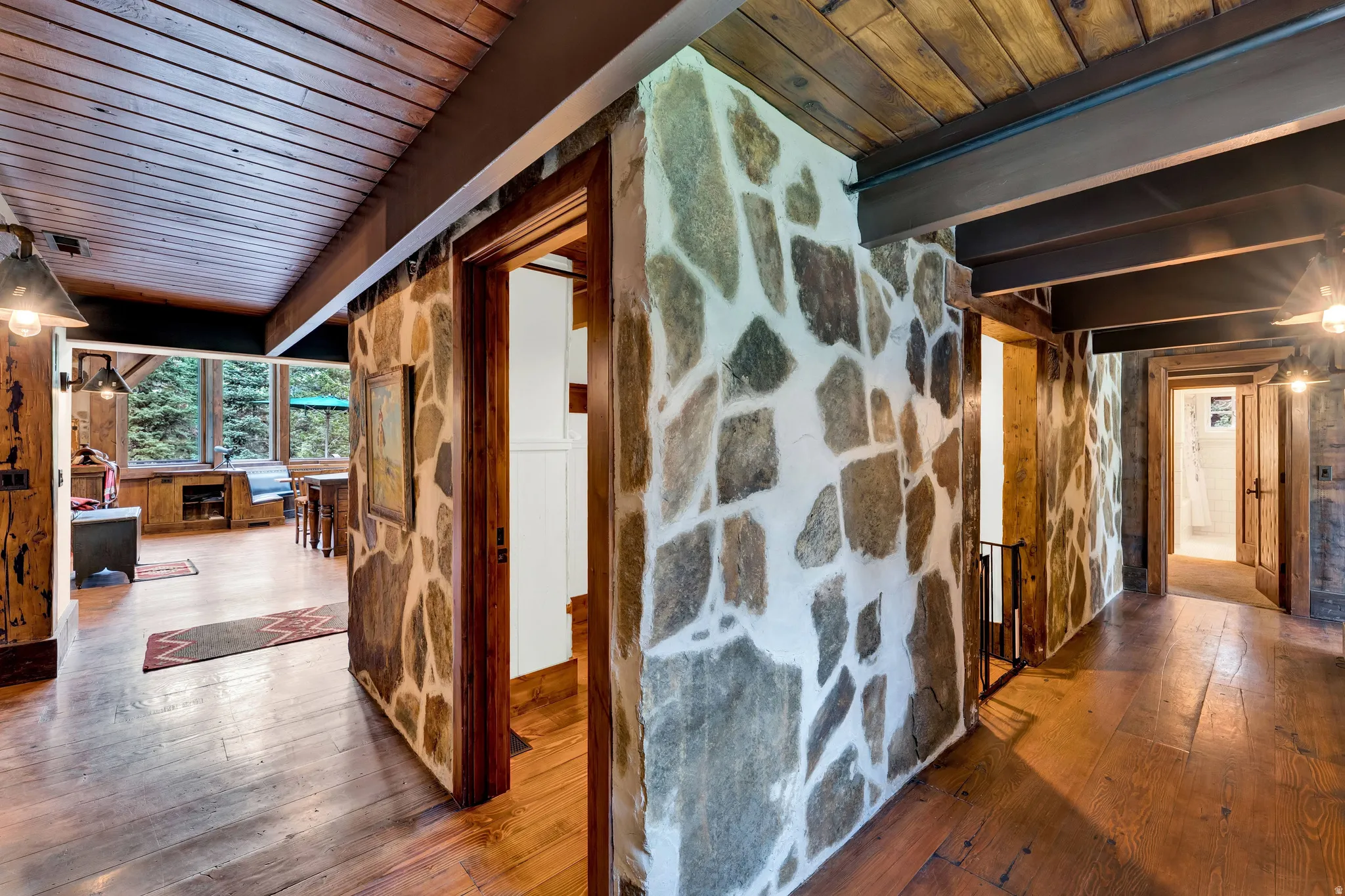 Striking interior hallway showcasing exposed stone accent walls with natural gray and white striations, warm wood-finish flooring, and vaulted wood-beamed ceilings