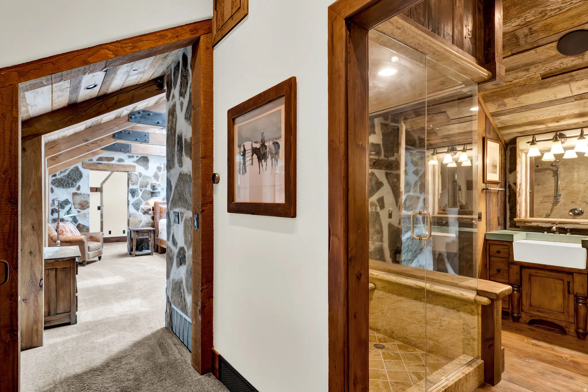 Elegant hallway showcasing rich wood-trimmed doorways and framed architectural details, leading to a spa-inspired bathroom featuring a walk-in shower with glass enclosure, warm wood cabinetry, and tile flooring