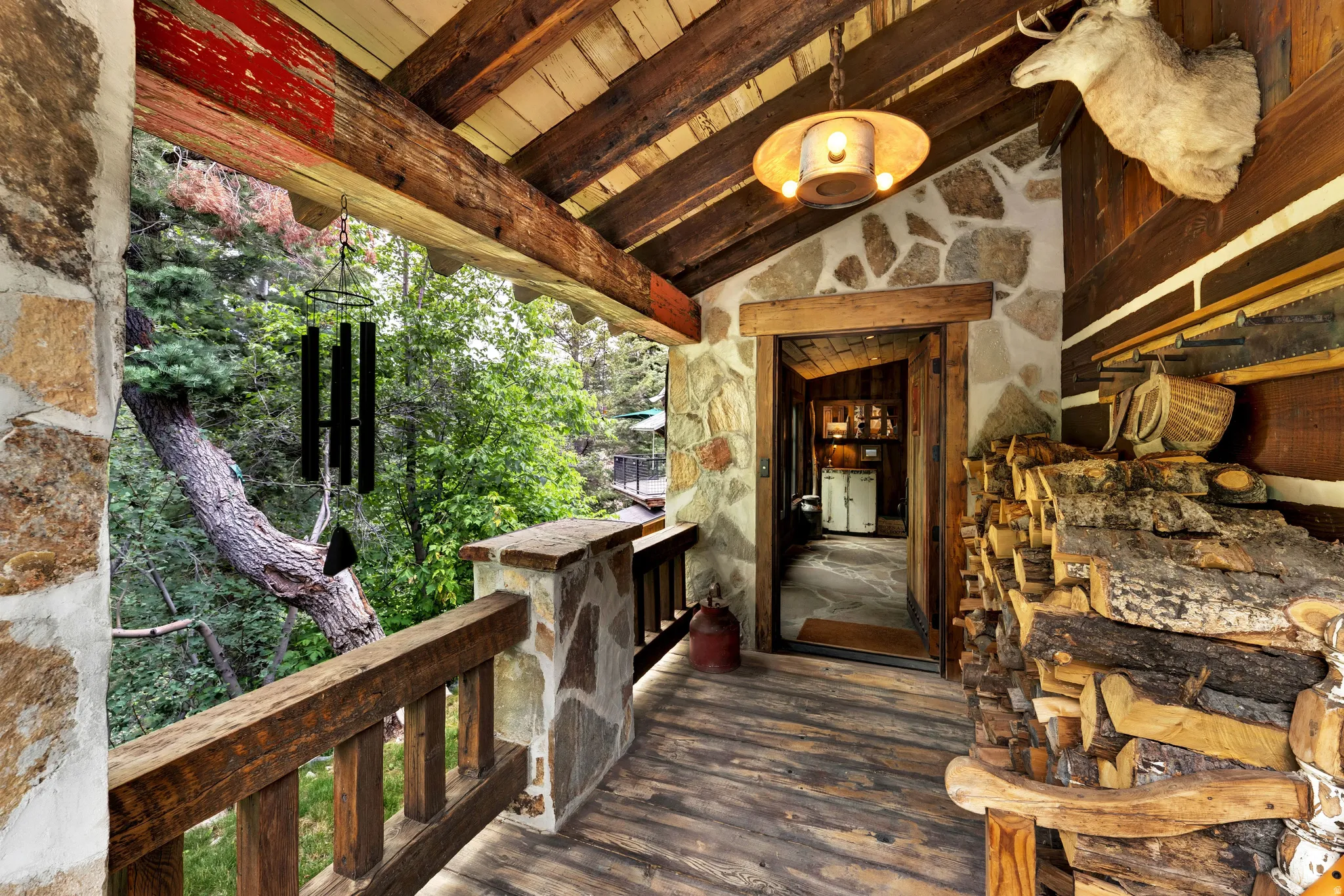 Rustic covered porch featuring exposed wood beam ceiling, wood-finish flooring, and natural stone exterior walls