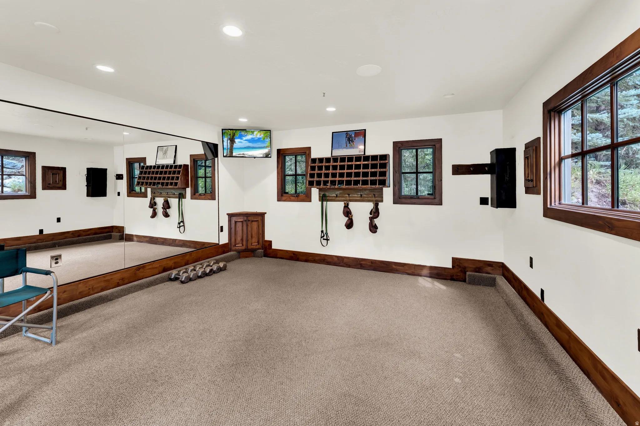 Spacious recreational room featuring recessed ceiling lighting, wood-trimmed windows with natural light, neutral carpet flooring, and wood-paneled wainscoting throughout
