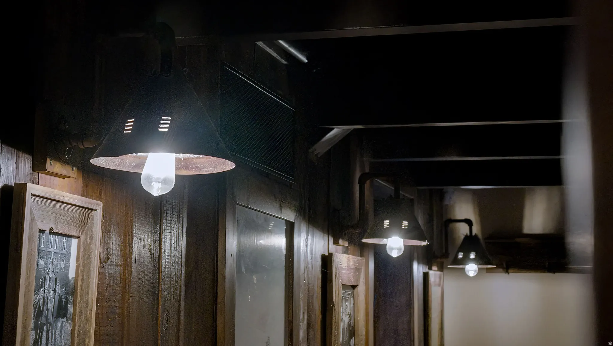 Hallway featuring industrial-style pendant lighting with brushed metal shades, wood-finish doors with frosted glass panels, and dark ceiling treatments creating a modern aesthetic