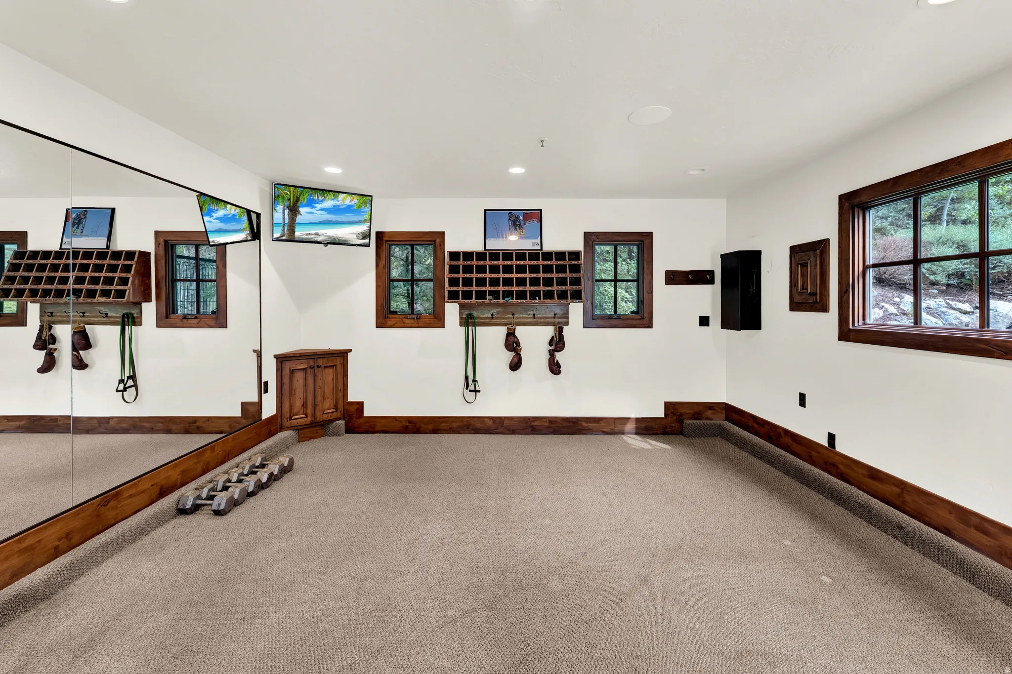 Carpeted room featuring a full-wall mirror, multiple built-in storage units, three windows with dark wood trim, and recessed ceiling lights