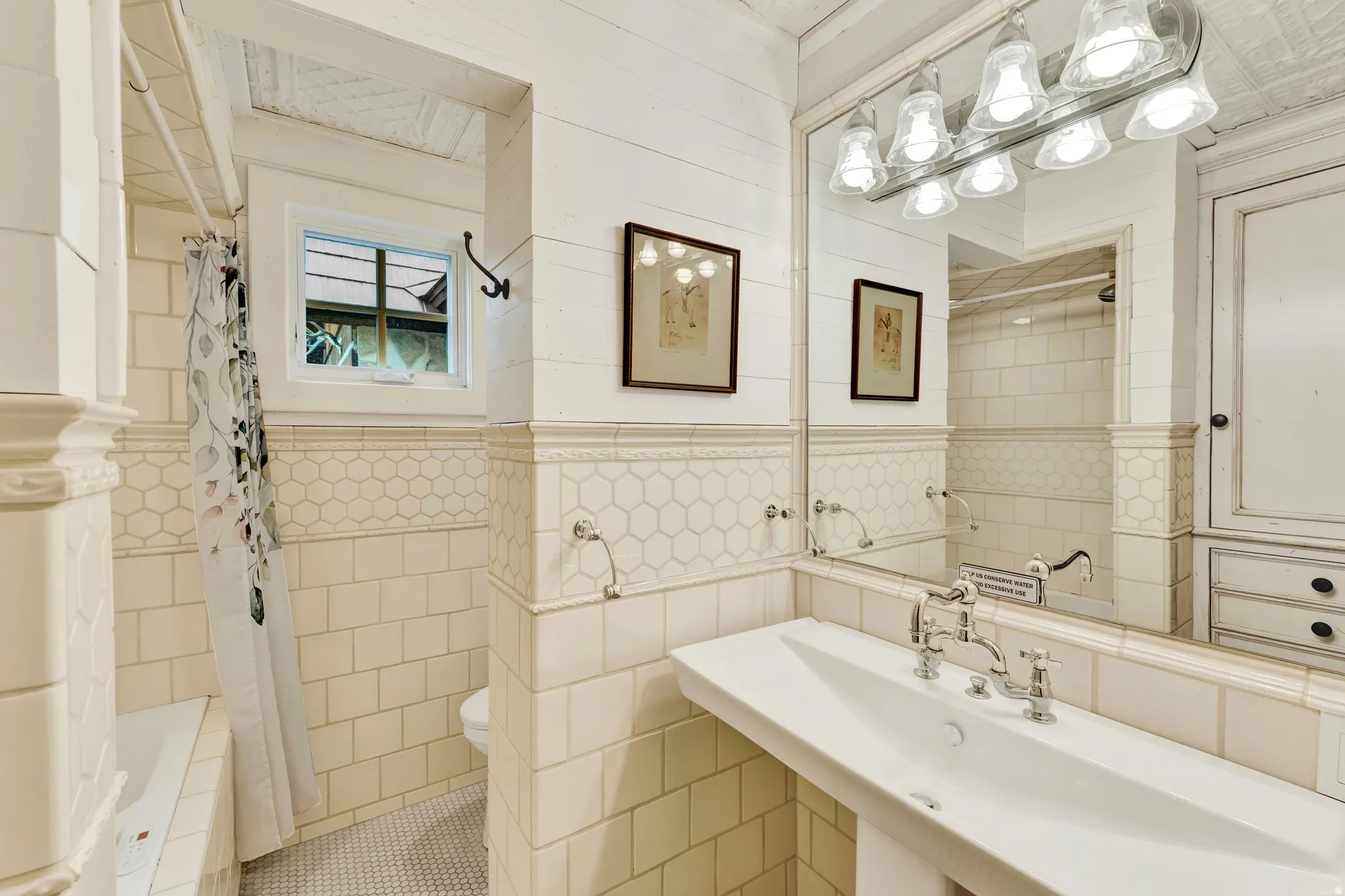 Classic bathroom featuring subway tile wainscoting, a dual-sink vanity with chrome bridge faucet and vintage-style hardware, large mirror with integrated lighting, and separate shower and toilet compartments