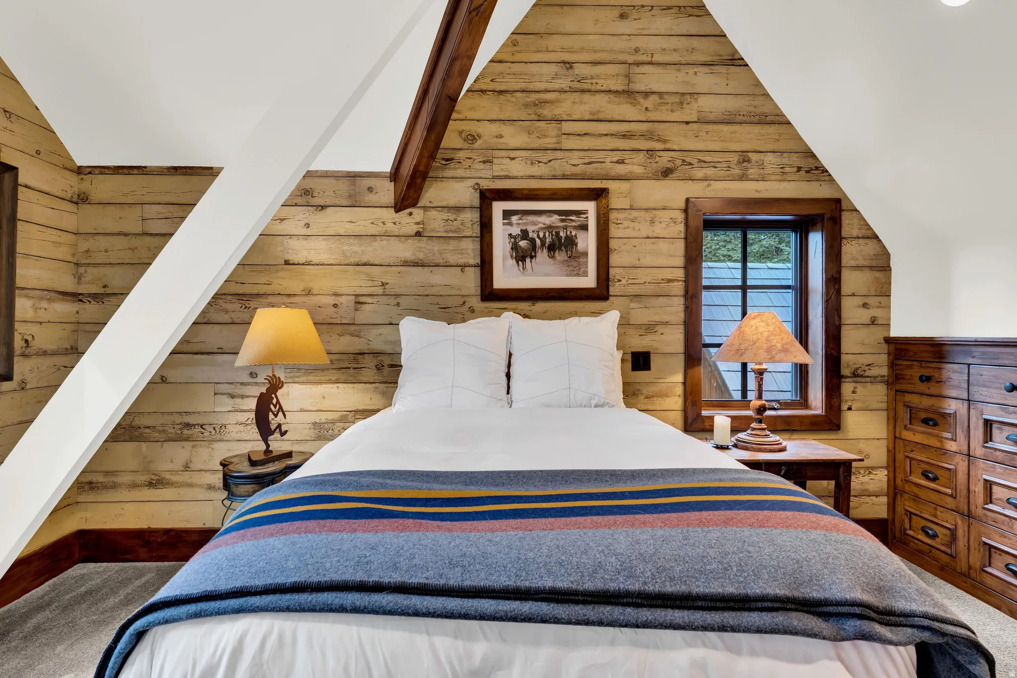 Charming bedroom retreat showcasing rustic wood plank walls, vaulted ceilings with exposed beam detailing, and abundant natural light from dual windows