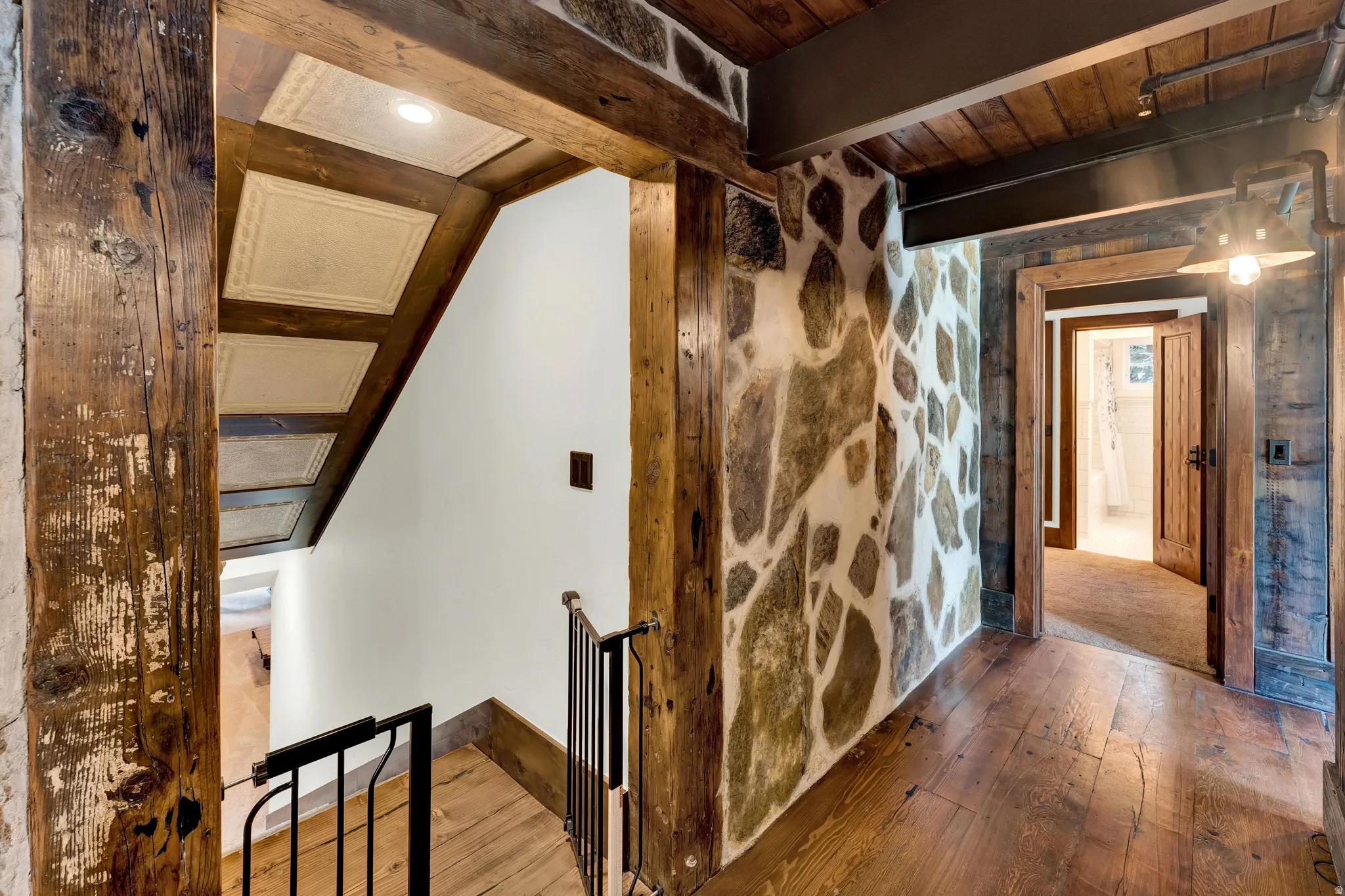 Rustic-modern interior featuring exposed timber beams, stone accent walls, and hardwood flooring throughout