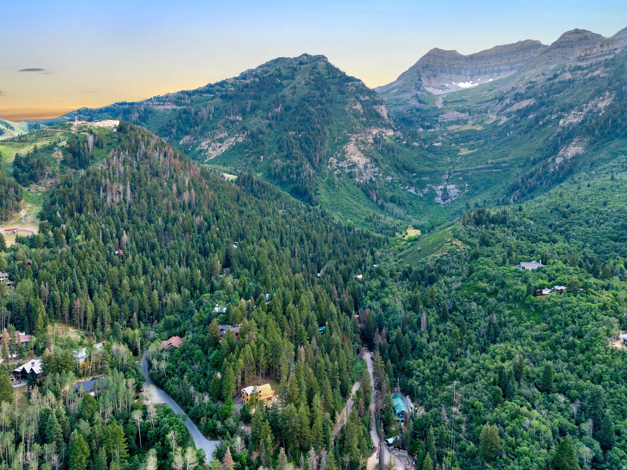 Expansive mountain landscape with diverse evergreen tree coverage and a distant waterfall feature