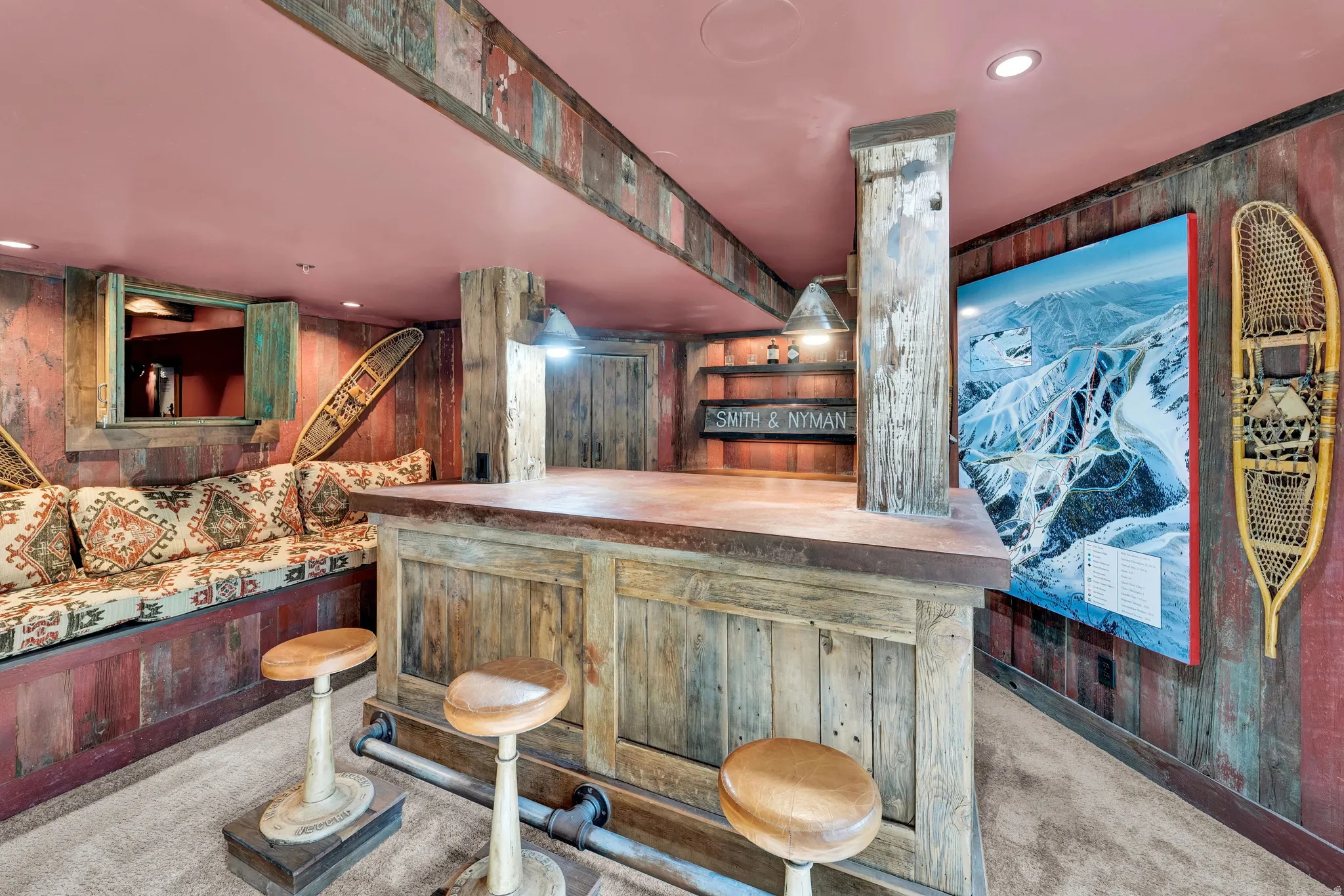 Finished Recreation Room featuring custom wood-paneled bar with seating for multiple guests, built-in shelving and cabinetry, recessed ceiling lighting, and large flat-screen television mounted on accent wall
