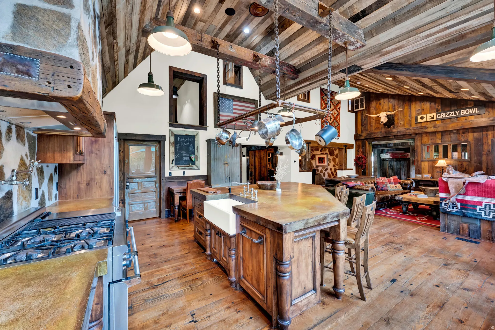 Rustic-modern kitchen anchored by a substantial wood-finish island with seating, featuring exposed beam ceiling, pendant lighting, and wood-finish flooring throughout