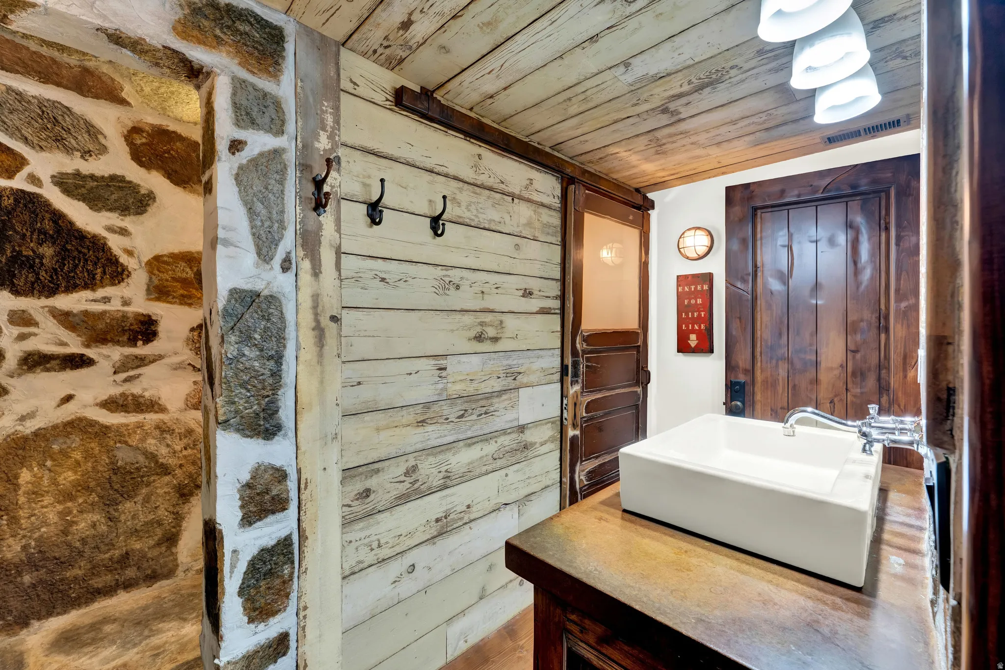 Spa-inspired primary bathroom featuring rustic stone accent wall, whitewashed shiplap paneling, and a modern rectangular vessel sink set atop a wood-finish vanity