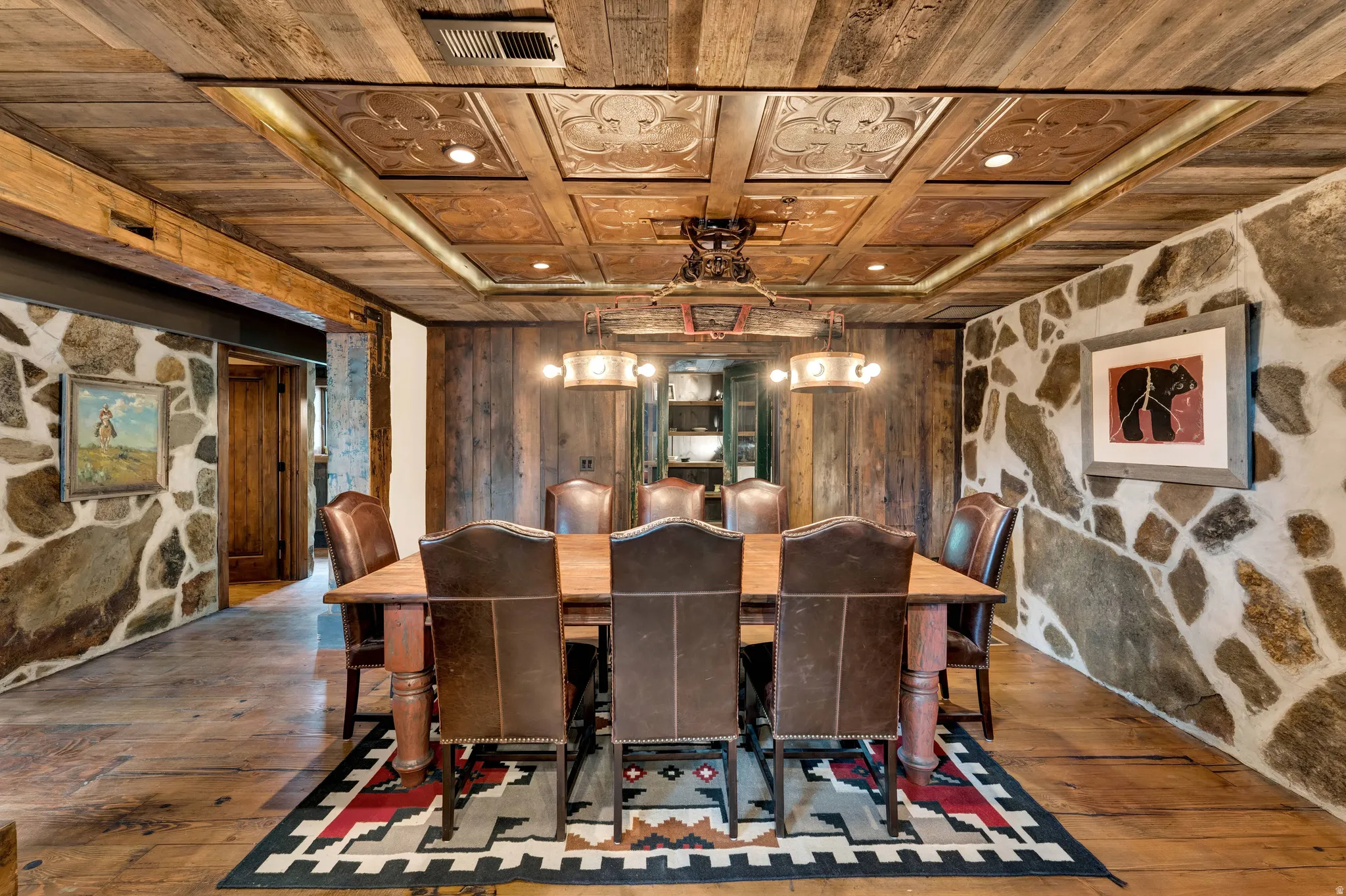 Formal dining room showcasing a coffered wood ceiling with recessed lighting, stone accent walls, hardwood flooring, and a geometric area rug anchoring the dining space