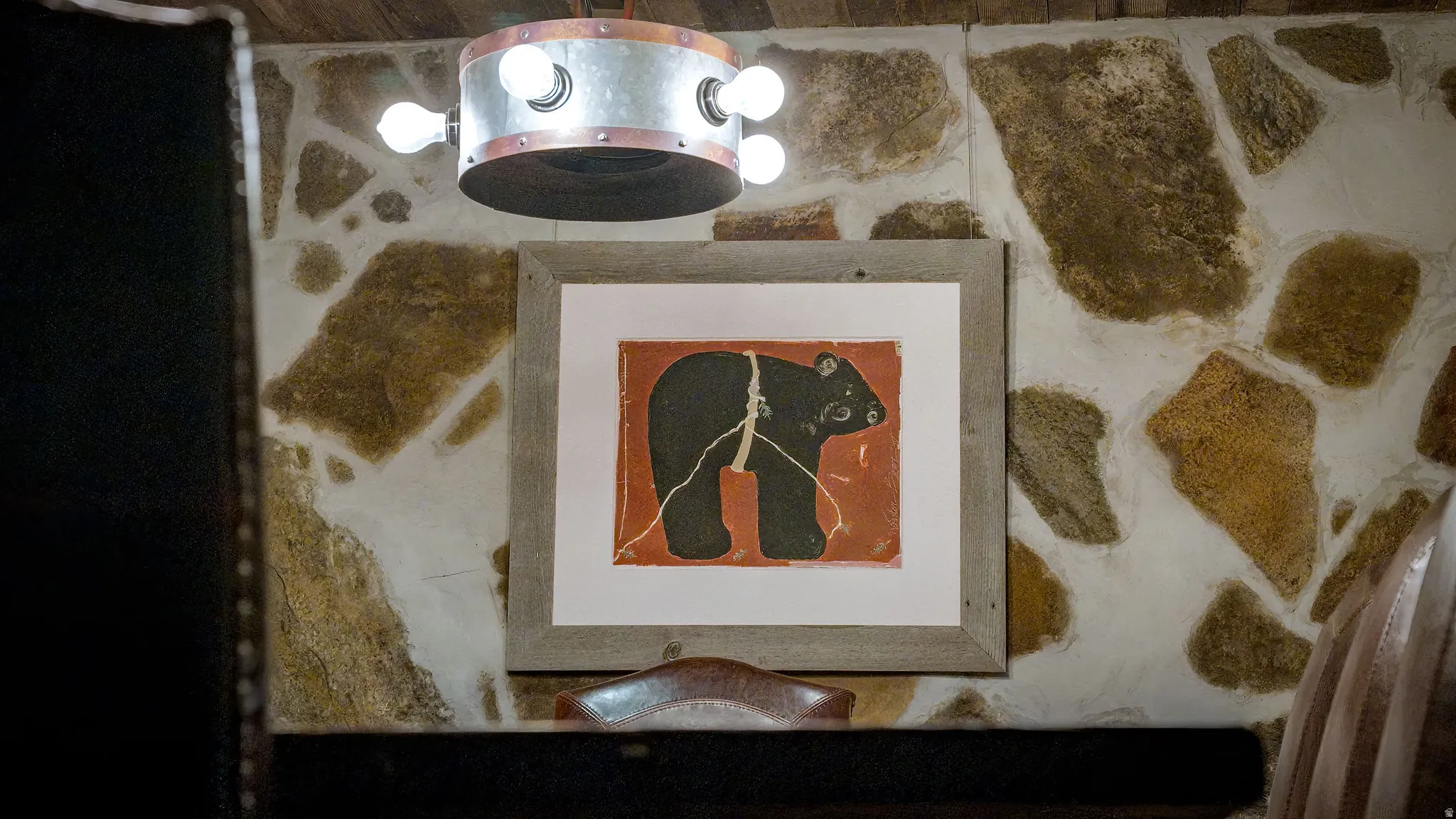Rough-hewn stone wall with light grout, wood-finish ceiling, and a rustic metal drum light fixture
