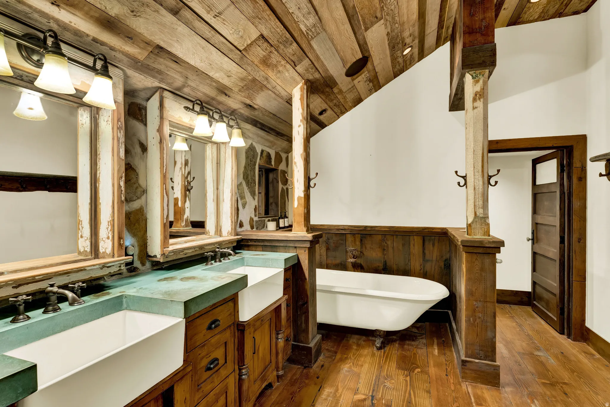 Spa-inspired master bathroom featuring dual vanities with green glass countertops and wood cabinetry, paired vessel sinks, and polished wood-finish flooring