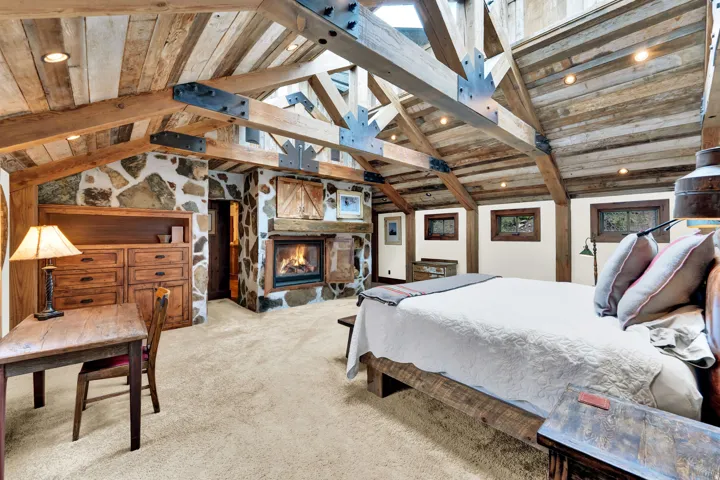 Spacious primary bedroom showcasing soaring vaulted ceilings with exposed wooden beams, skylights flooding the space with natural light, and a wood-burning fireplace