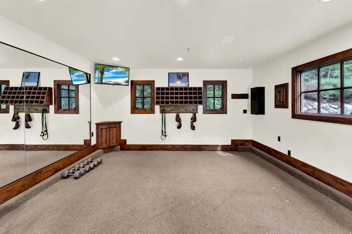 Carpeted room featuring a full-wall mirror, multiple built-in storage units, three windows with dark wood trim, and recessed ceiling lights