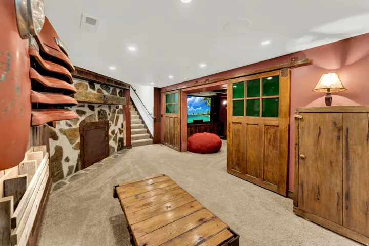 Recreation space featuring a stone accent wall with a wood beam mantel, carpeted flooring, and recessed lighting