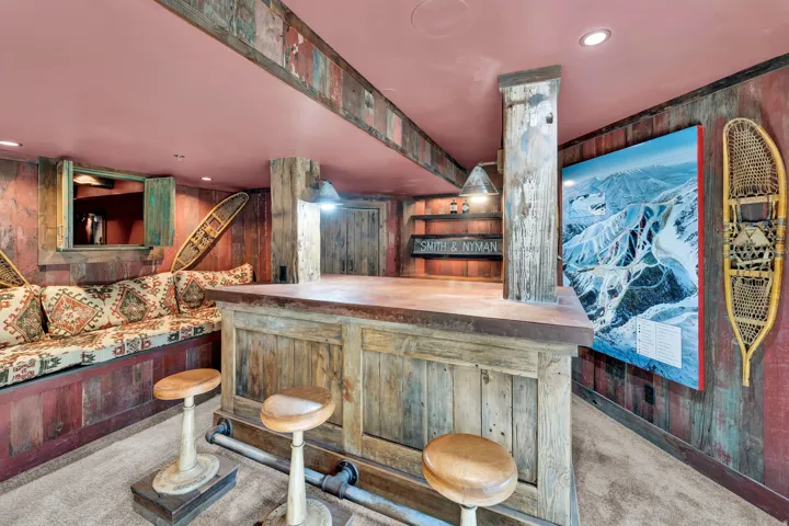 Finished Recreation Room featuring custom wood-paneled bar with seating for multiple guests, built-in shelving and cabinetry, recessed ceiling lighting, and large flat-screen television mounted on accent wall