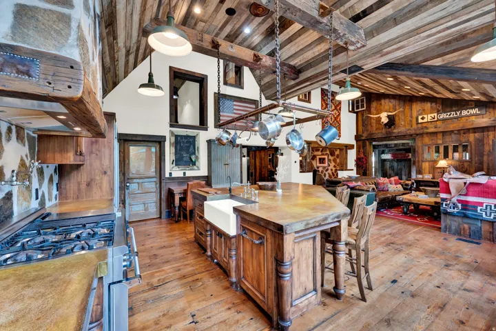 Rustic-modern kitchen anchored by a substantial wood-finish island with seating, featuring exposed beam ceiling, pendant lighting, and wood-finish flooring throughout