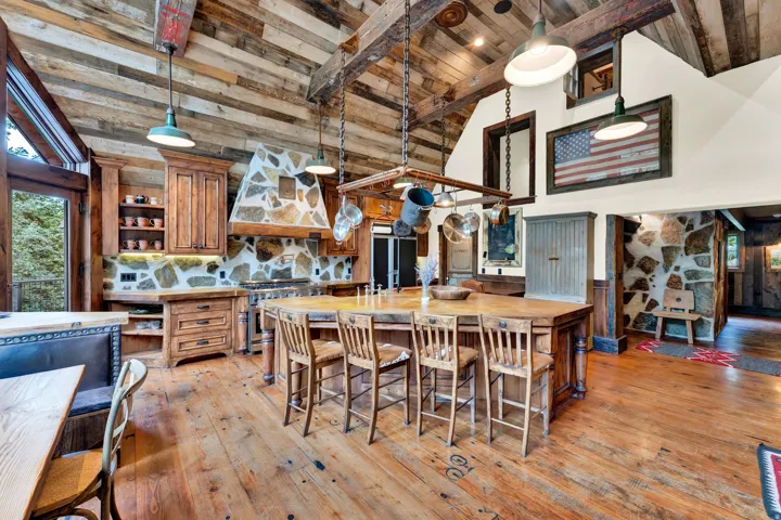 Expansive kitchen featuring wood-finish flooring, stone backsplash, rich wood cabinetry, and a substantial center island with seating