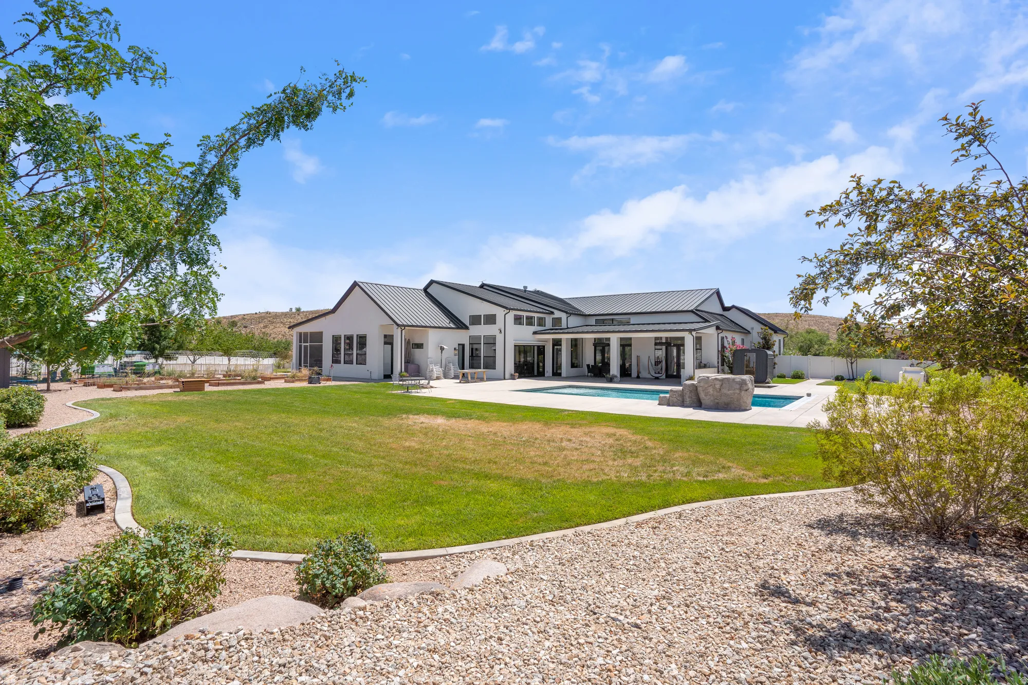 Expansive backyard featuring a manicured lawn, a swimming pool with rock features, and a spacious concrete patio