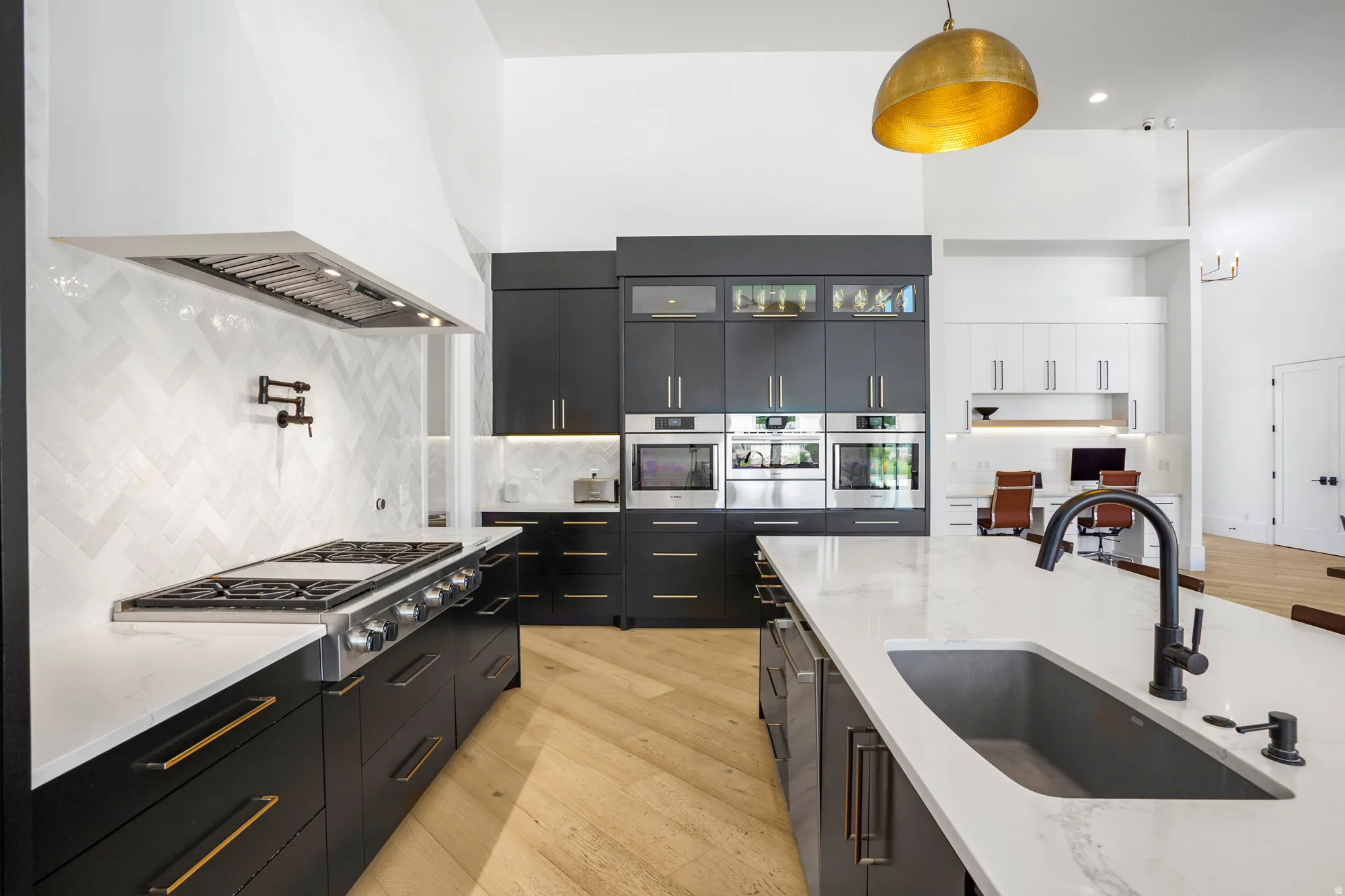 Modern kitchen featuring sleek black cabinetry with brushed gold hardware, white quartz countertops, and a large waterfall-edge island with undermount sink