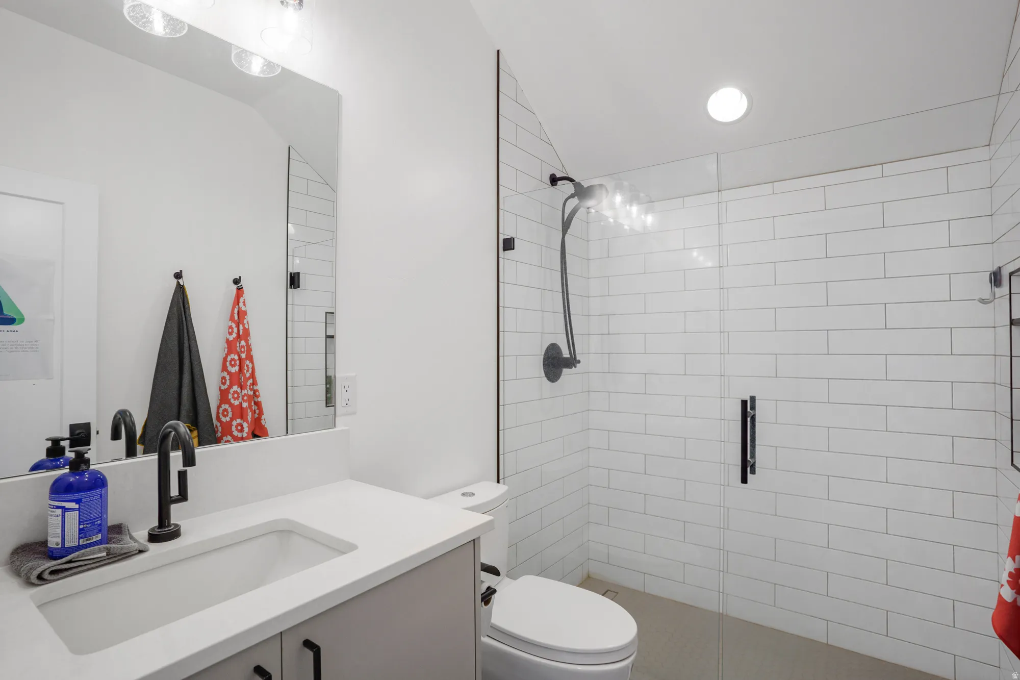 Modern bathroom featuring a glass-enclosed shower with white subway tile, a vanity with a white countertop and integrated sink, and black matte fixtures