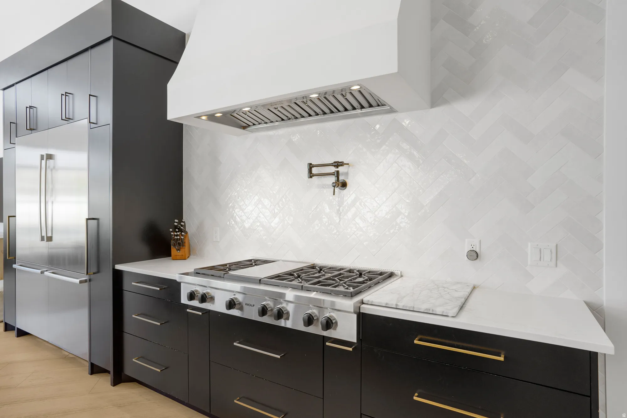 Gourmet kitchen featuring a professional-grade gas range, herringbone tile backsplash, integrated stainless steel refrigerator, white countertops, and dark cabinetry