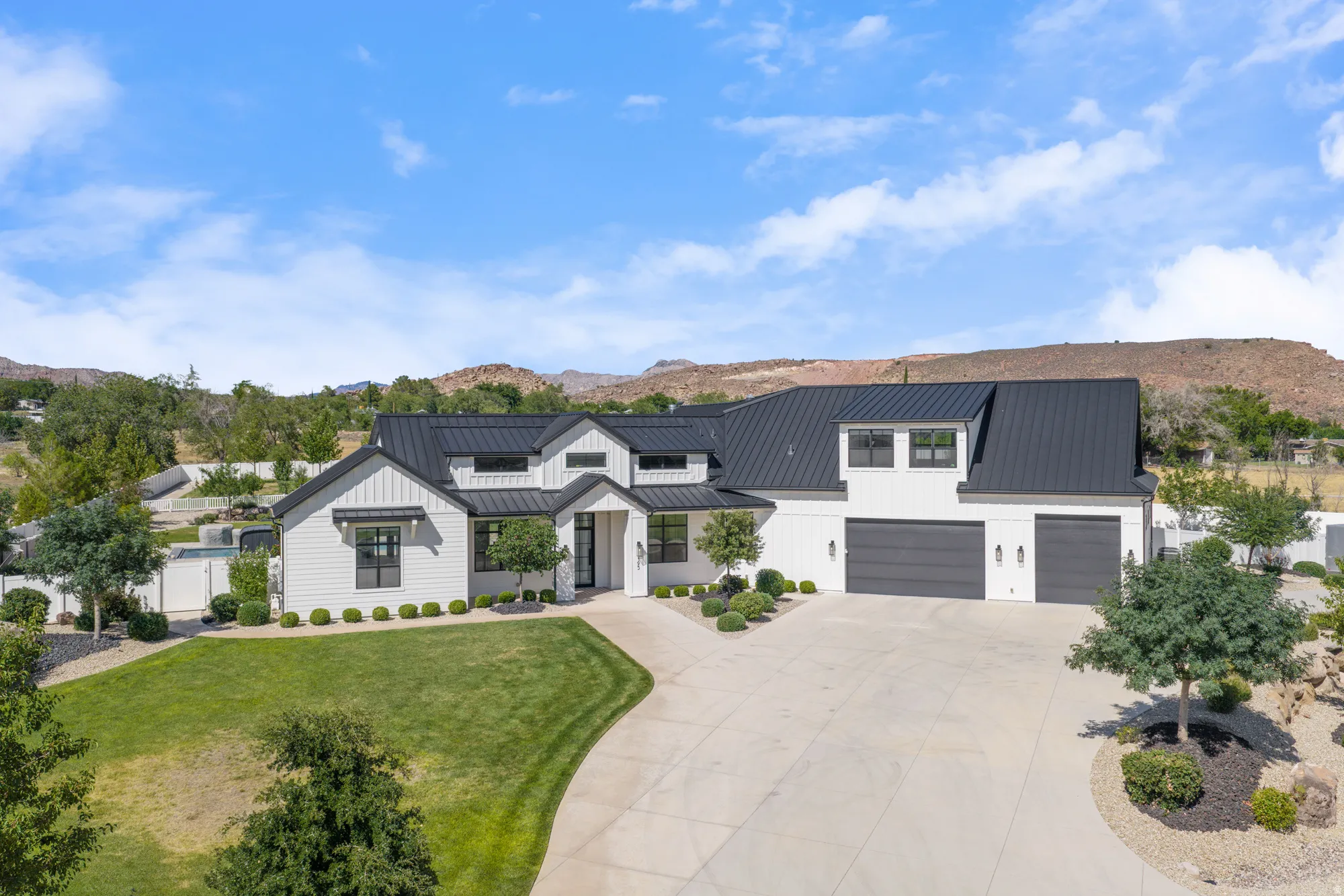 Modern farmhouse residence showcasing a clean-lined white exterior with black metal roof accents, dual garage with white paneling, and architectural detailing including gabled rooflines and substantial driveway