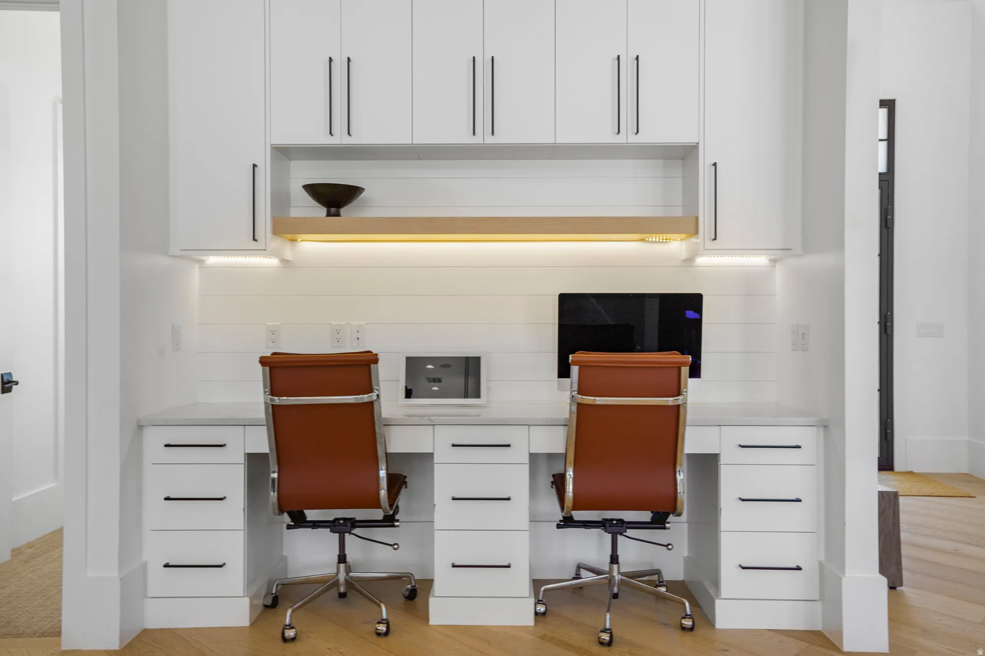 Dual-desk home office featuring built-in white cabinetry with ample storage drawers, integrated task lighting with warm-toned LED strips, and a spacious work surface