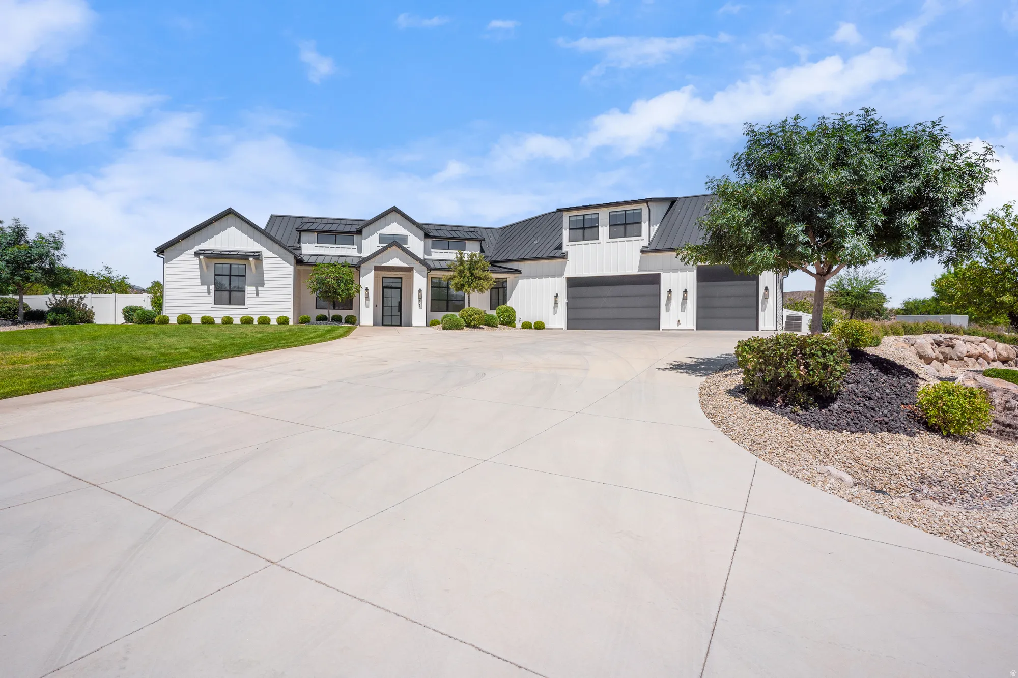 Striking Contemporary Residence featuring a Spacious Concrete Driveway, Dual-Bay Garage with Dark Finishes, Manicured Lawn with Mature Landscaping, Architectural Stone Hardscaping with Native Plantings, and Clean-lined Exterior Elevation with Peaked Roofl