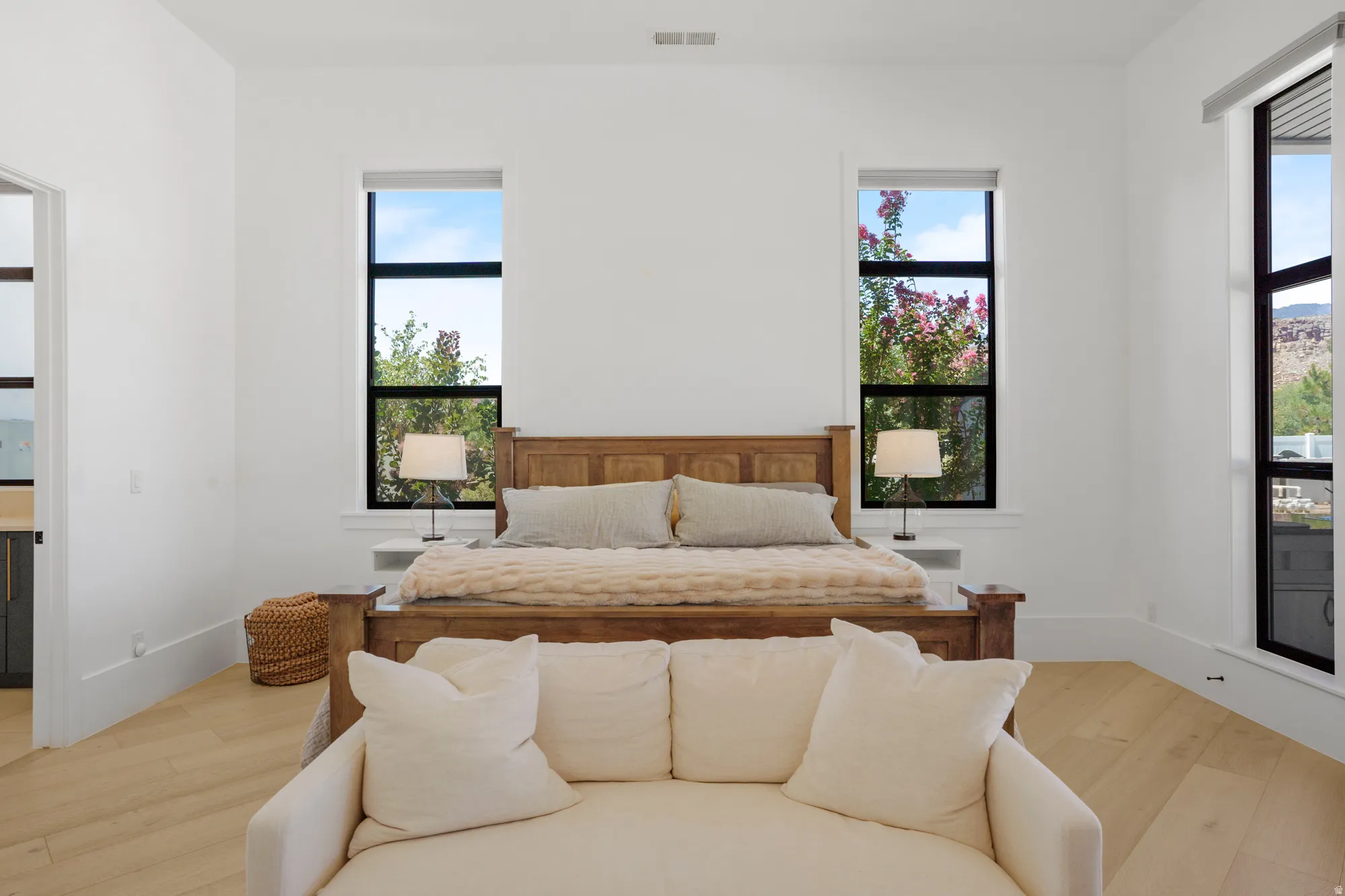 Bright, light-filled bedroom featuring expansive windows with black-frame detailing and natural wood flooring throughout