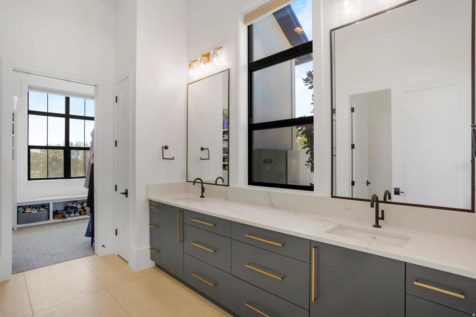 Spa-inspired primary bathroom showcasing a dual-vanity layout with charcoal cabinetry, brass hardware accents, and a white quartz countertop