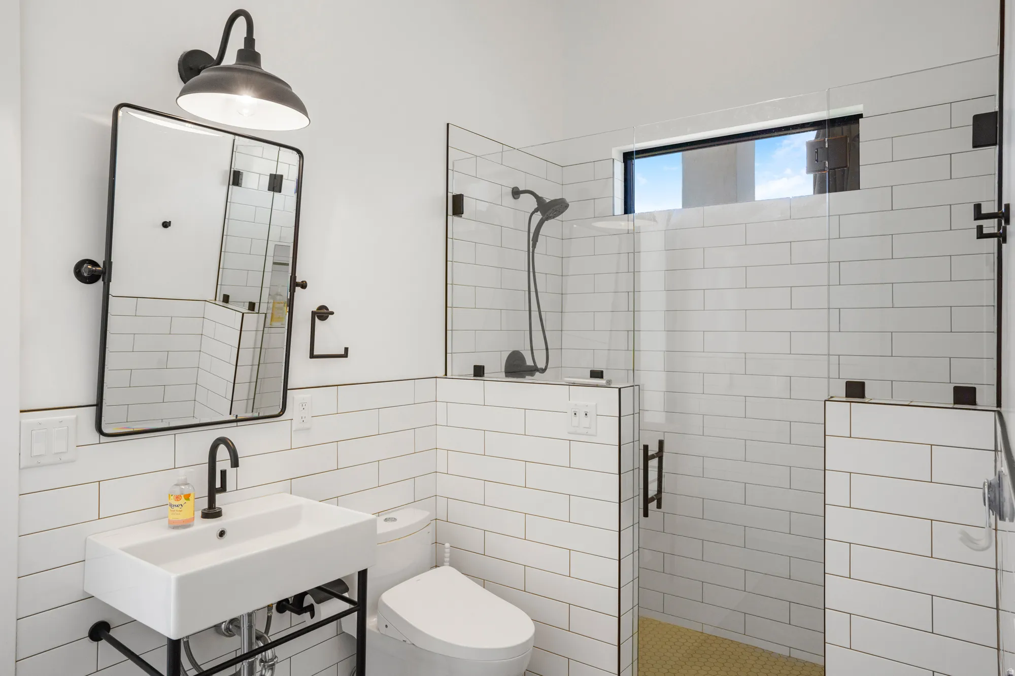 Bathroom featuring white subway tile walls, a wall-mounted rectangular sink with a matte black faucet, and a black-framed mirror
