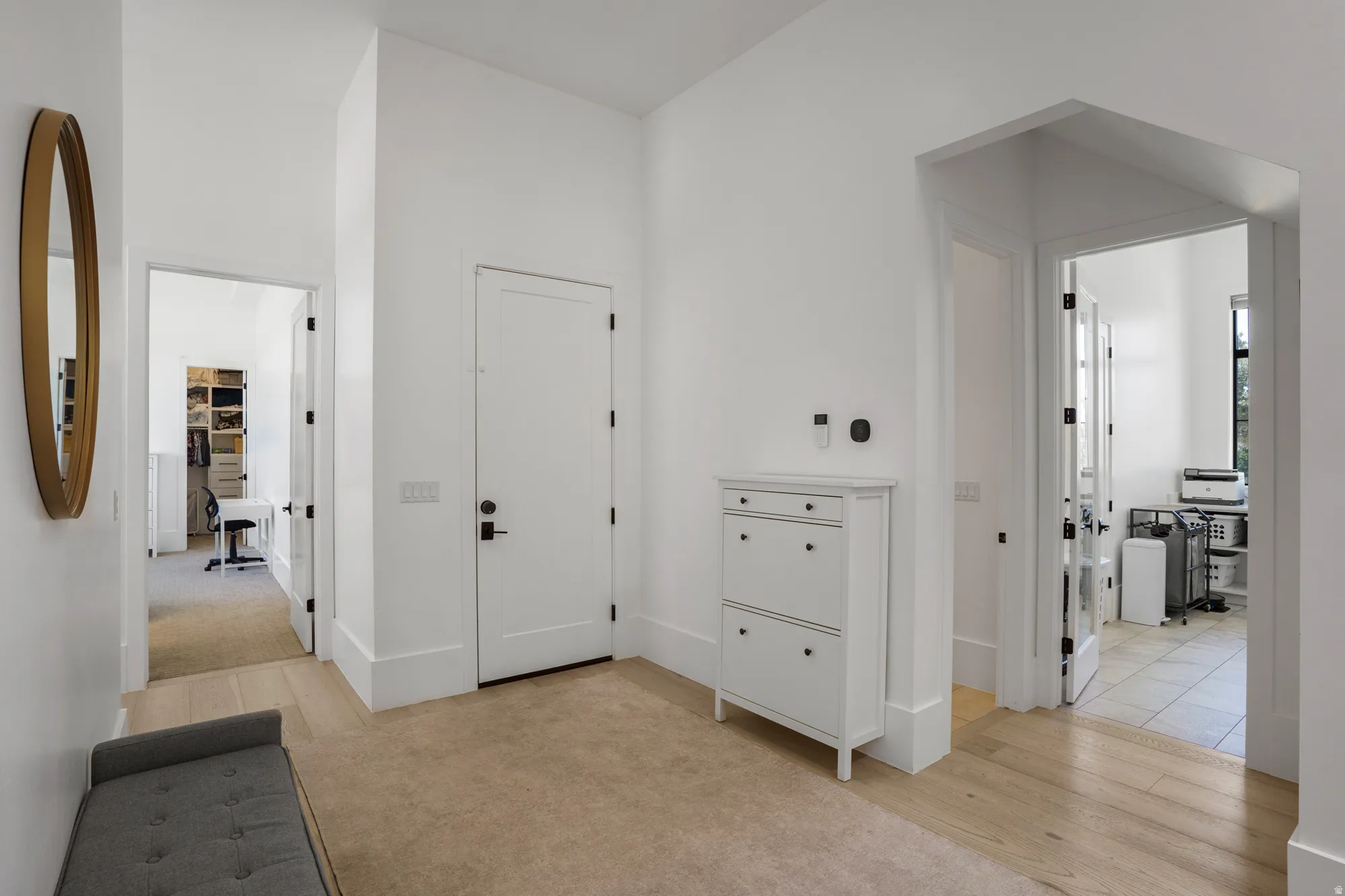 Bright foyer showcasing gleaming wood-finish flooring, white shaker-style doors with black hardware, and abundant natural light