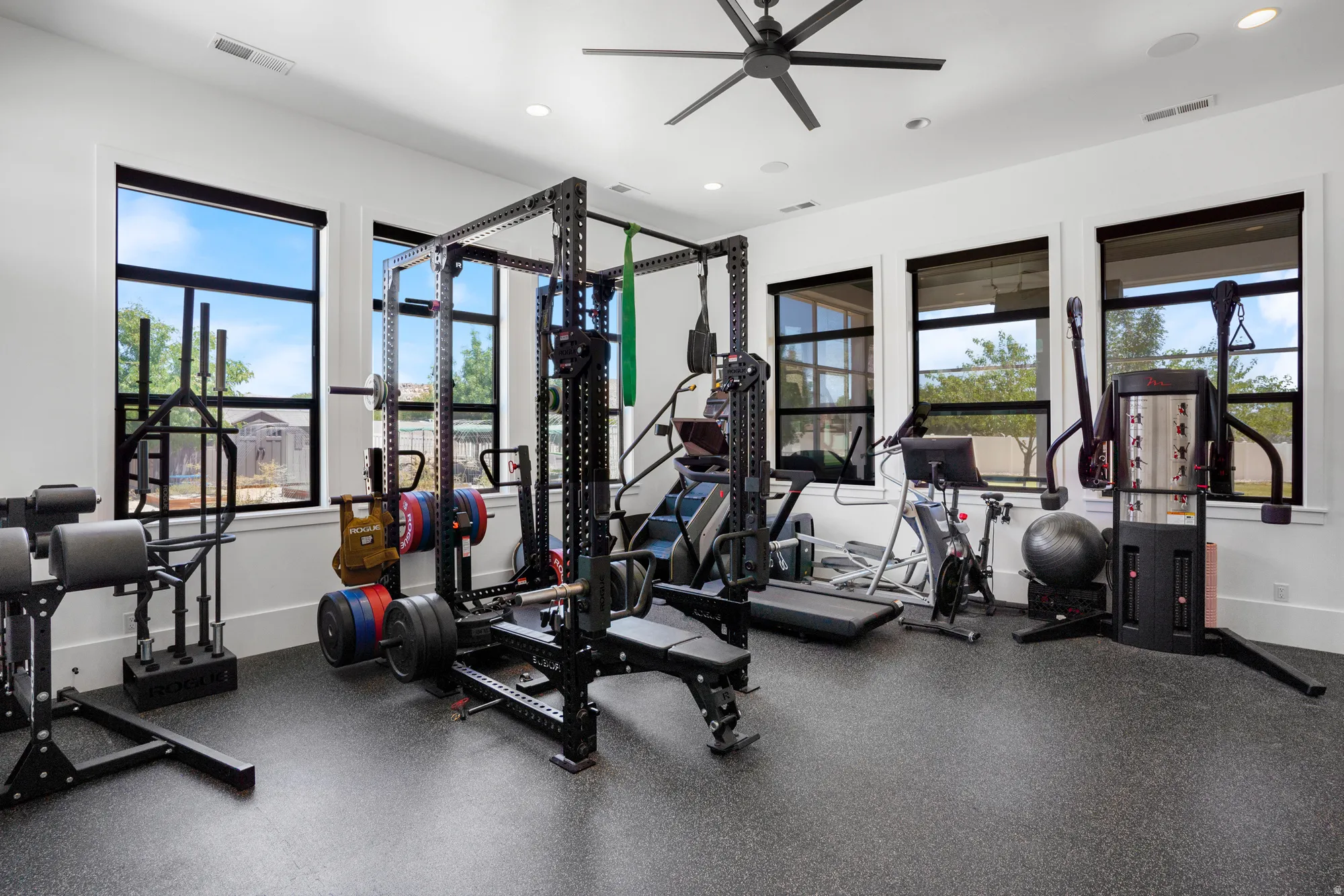 Dedicated fitness space featuring a rubber flooring system, multiple large windows with black framing, recessed lighting, and a ceiling fan