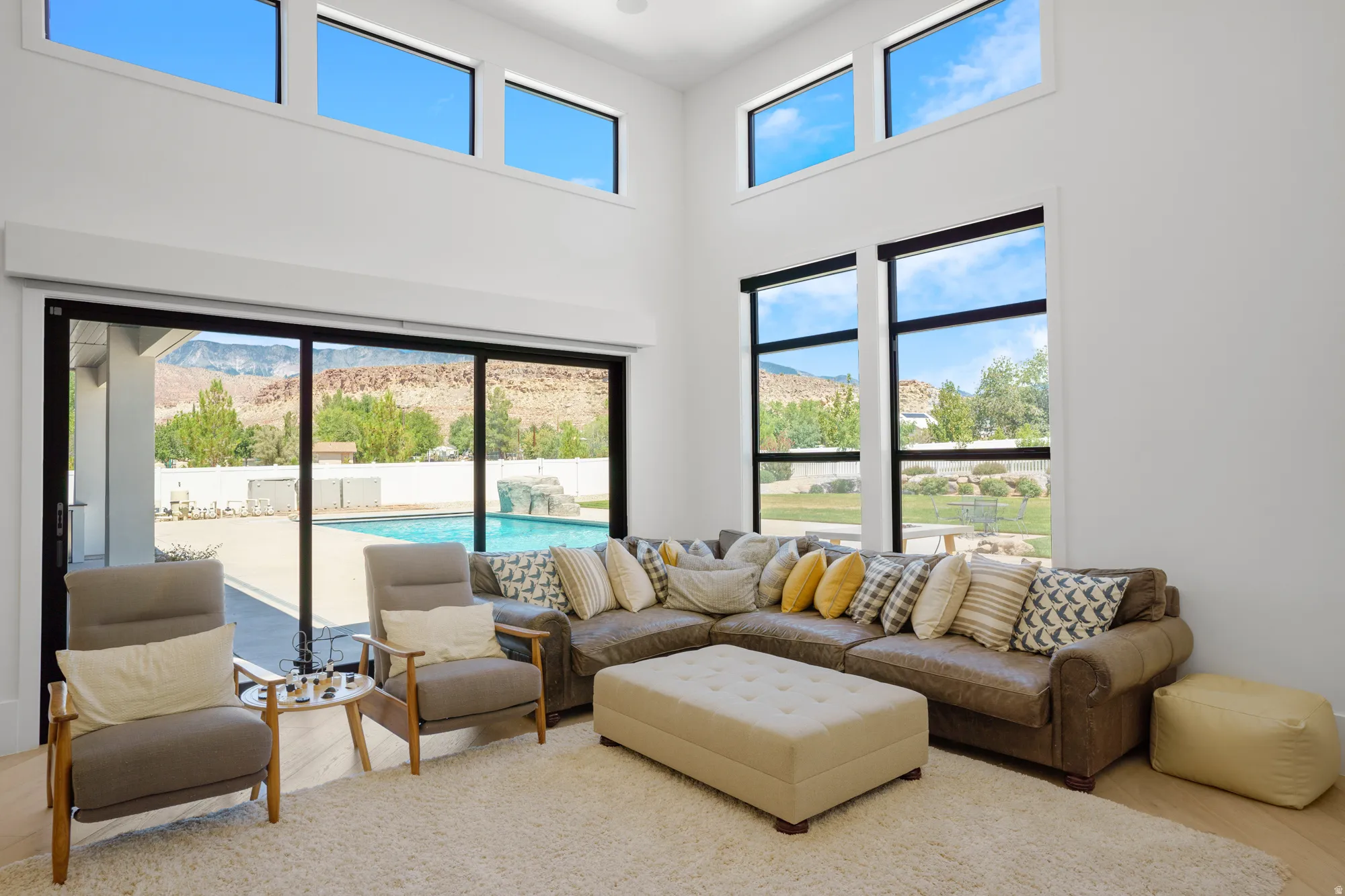 Bright, light-filled living room showcasing floor-to-ceiling windows, clerestory glazing, and sliding glass doors opening to pool and outdoor entertaining spaces