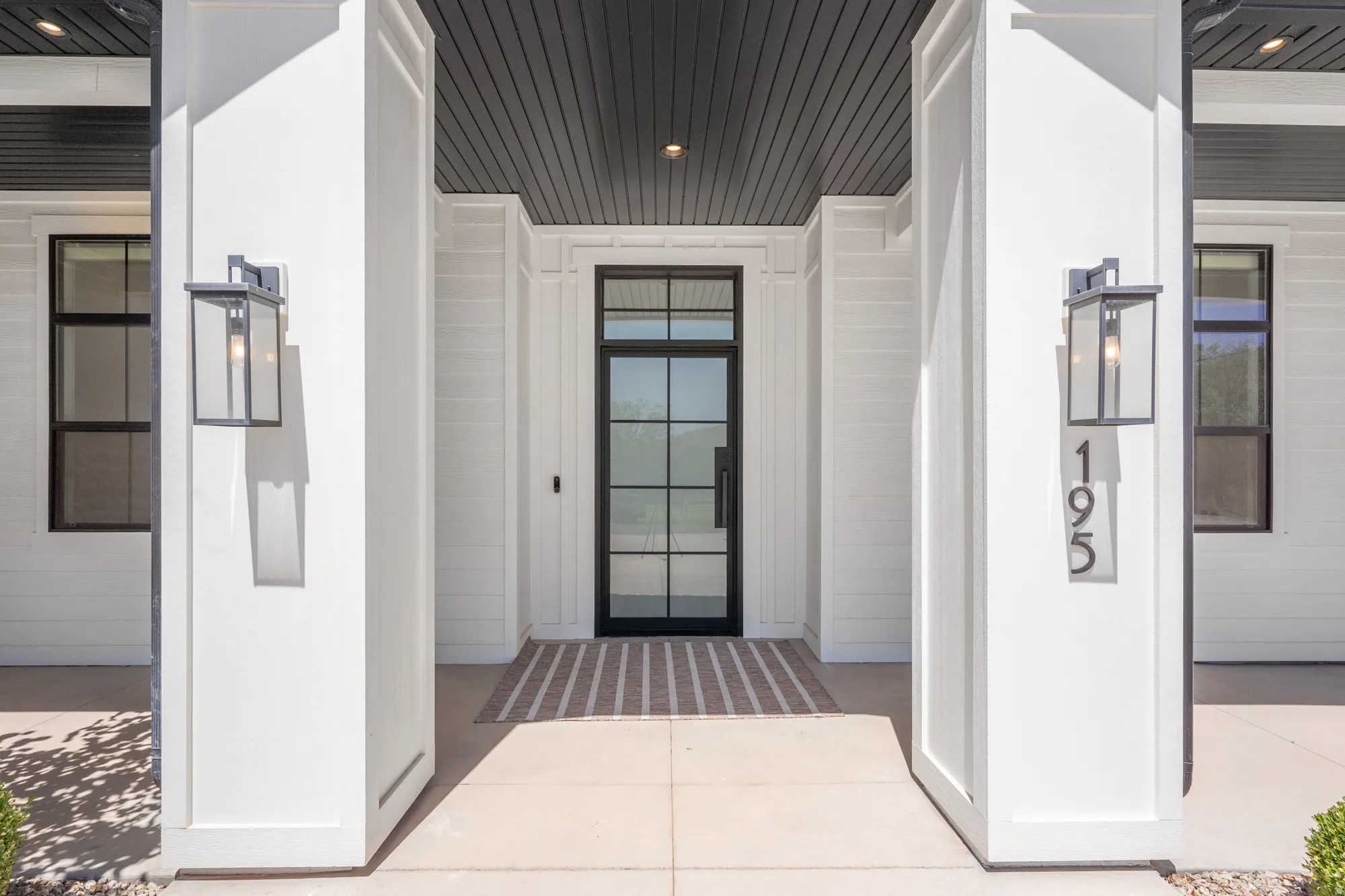 Modern farmhouse entry featuring a covered portico with symmetrical white columns and black-framed glass door