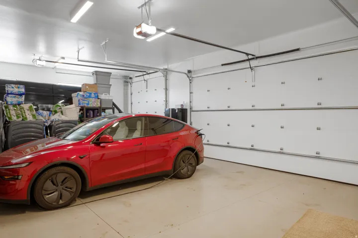 Spacious attached garage featuring epoxy-coated concrete flooring, overhead garage door with automatic opener, fluorescent ceiling lighting, and ample storage potential