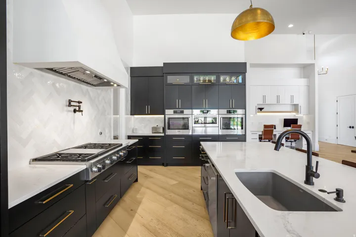 Modern kitchen featuring sleek black cabinetry with brushed gold hardware, white quartz countertops, and a large waterfall-edge island with undermount sink