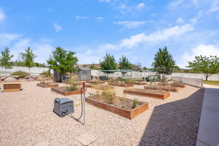 Spacious gravel yard featuring multiple raised garden beds, a storage shed, and a white picket fence perimeter