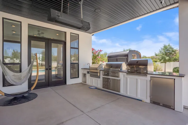 Covered outdoor kitchen featuring stainless steel appliances, including dual grills and a built-in refrigerator, paired with white cabinetry and a dark countertop