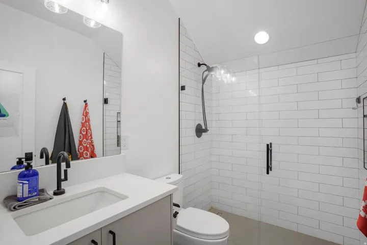 Modern bathroom featuring a glass-enclosed shower with white subway tile, a vanity with a white countertop and integrated sink, and black matte fixtures