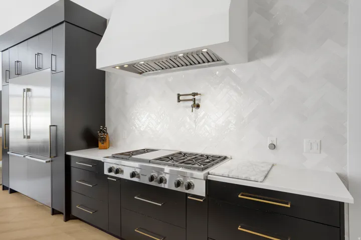Gourmet kitchen featuring a professional-grade gas range, herringbone tile backsplash, integrated stainless steel refrigerator, white countertops, and dark cabinetry